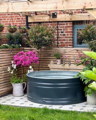 Black colored stock tank pool positioned on tiles and fencing behind it