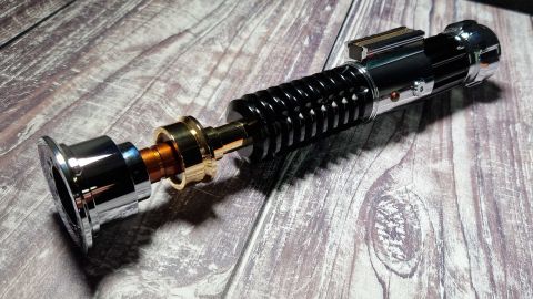 The hilt of the SabersPro Obi Wan EP3 on a wooden surface