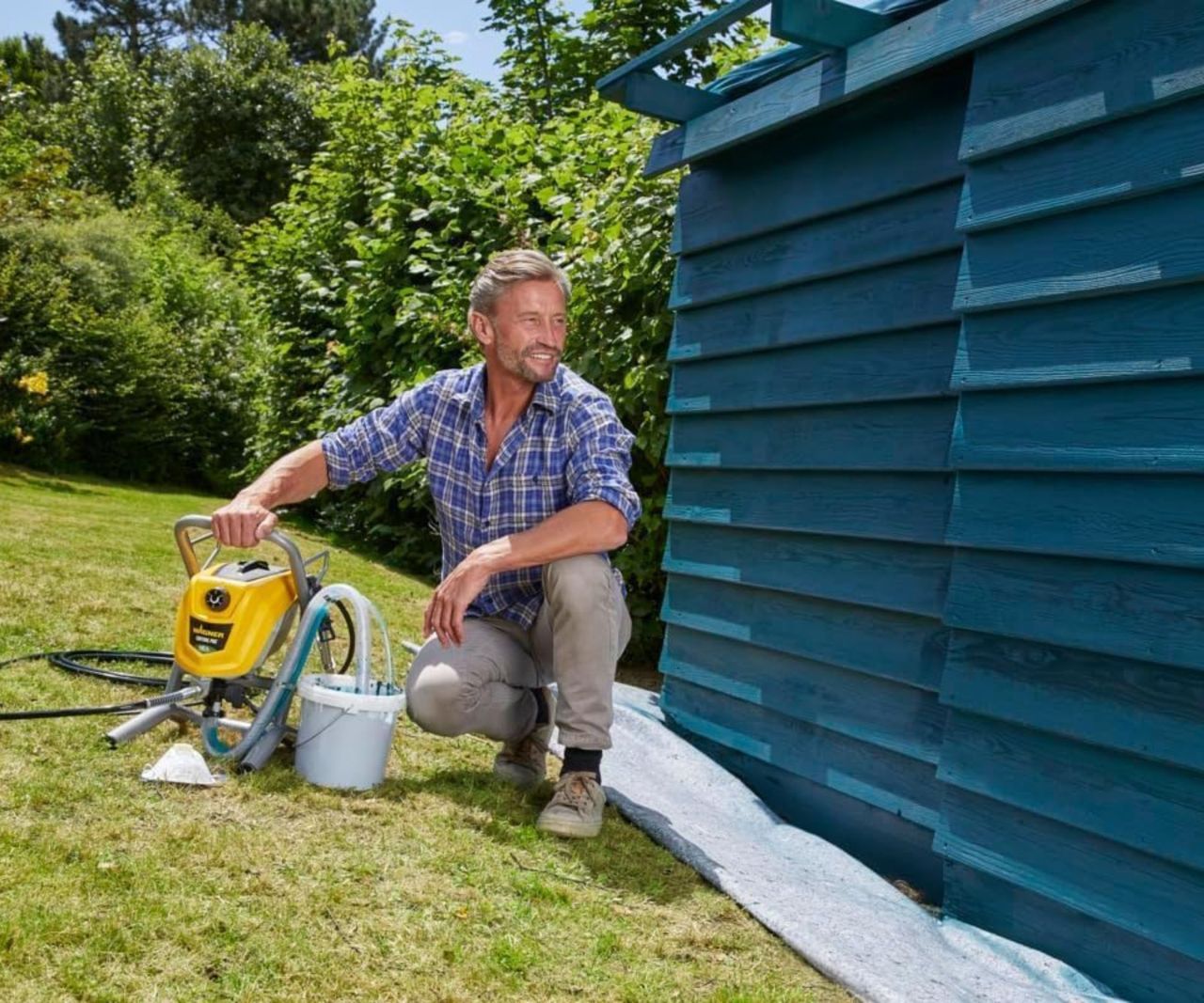 WAGNER ControlPro 250M Airless Paint Sprayer on the ground next to painted shed