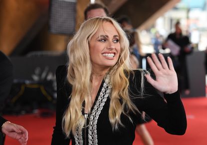 Rebel Wilson waving from the red carpet.