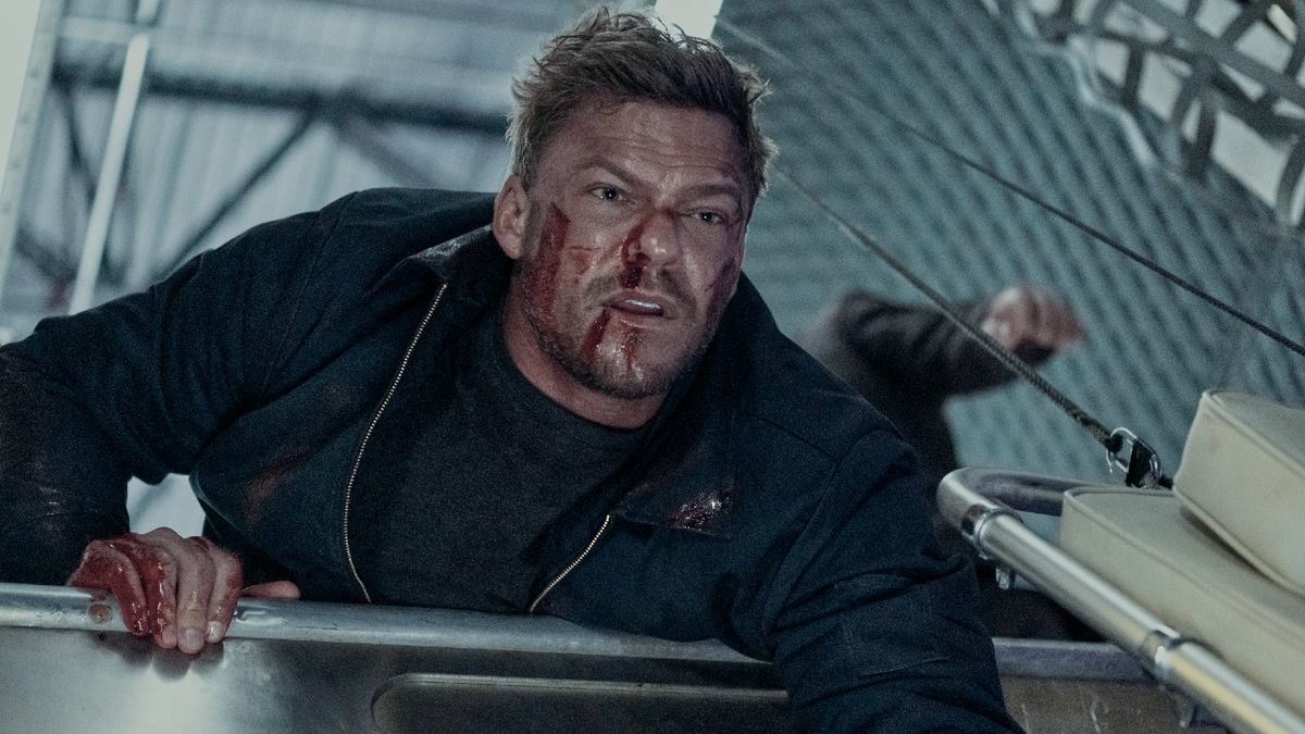 Alan Ritchson as Jack Reacker leaning over something with a bloody face and bloody left hand.