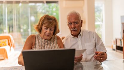 An older couple works on financial paperwork at their kitchen table.