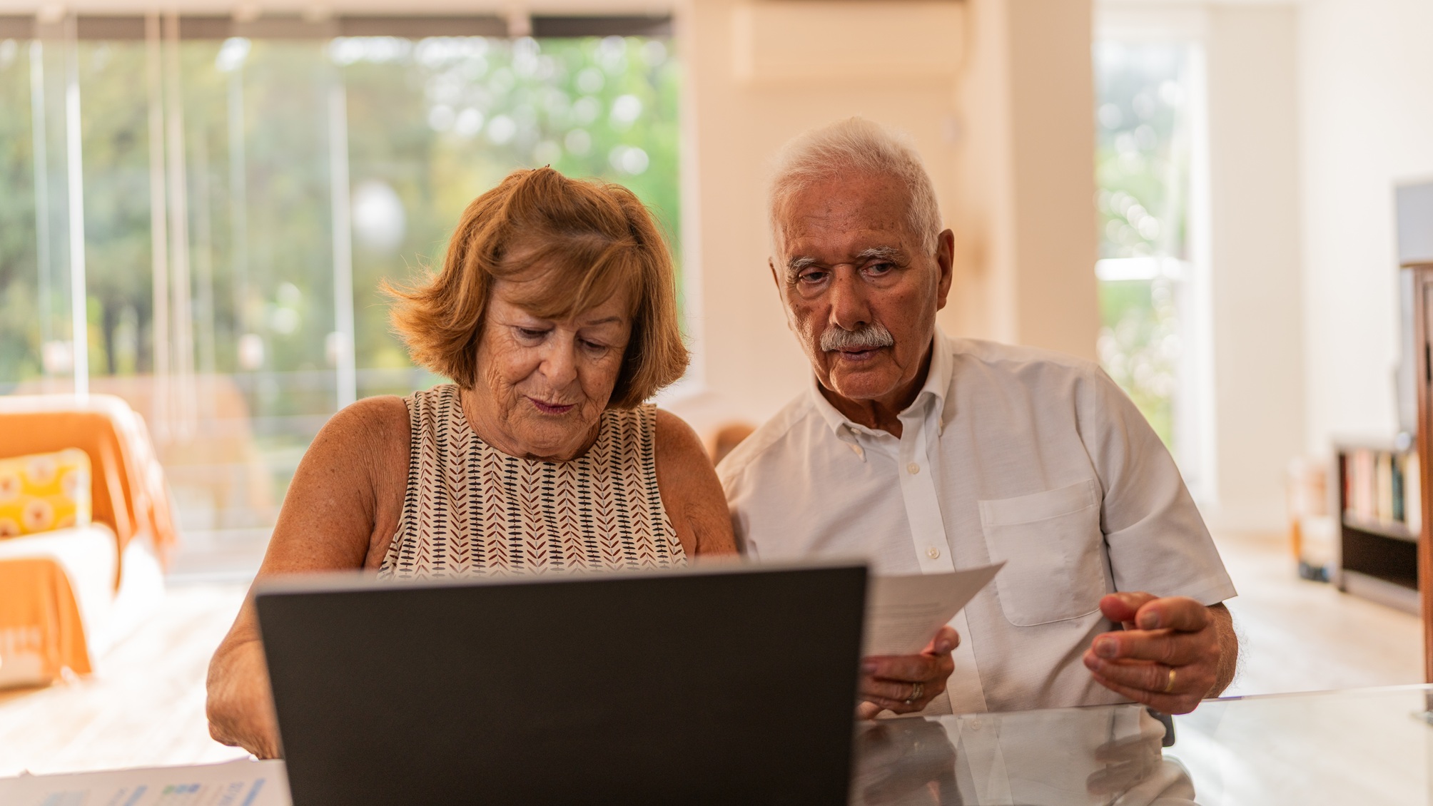 An older couple works on financial paperwork at their kitchen table.