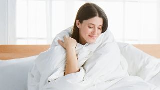 Woman sitting on bed wrapped in Avocado down duvet