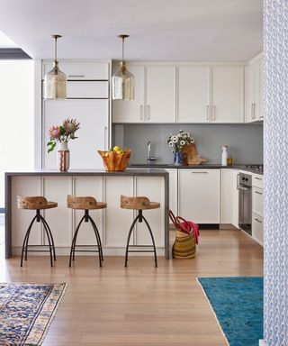 modern white kitchen with island, wooden barstools and glass pendants