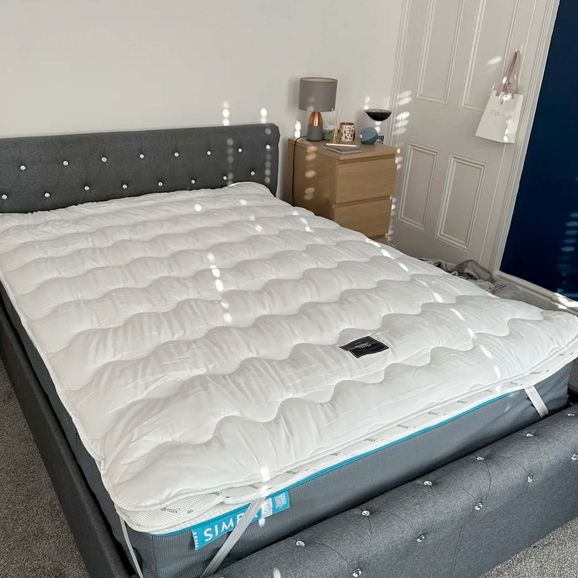 The Silentnight Airmax mattress topper attached to a mattress on a grey upholstered bed in a bedroom