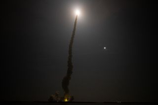 NASA's SLS rocket heads towards deep space as the moon shines beside its smoke trail in the night sky.