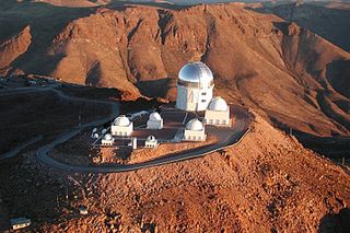 An aerial photo of the Cerro Tololo Inter-American Observatory (CTIO) atop Cerro Tololo in Chile. The Dark Energy Camera, the instrument at the heart of the Dark Energy Survey, is mounted onto the Victor Blanco 4-meter telescope, the largest telescope building on site and also easily identifiable because of its shiny dome.