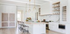 A luxury spacious white kitchen with an island, a marble splashback and light wooden finishes 