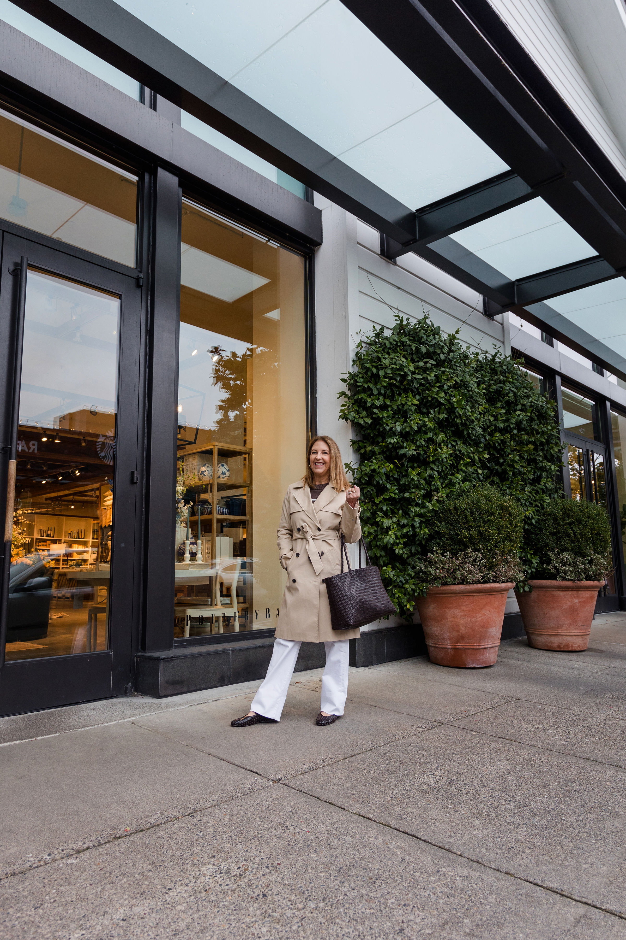 Um estilista Nordstrom usando um casaco bronzeado, jeans branco e apartamentos de balé.