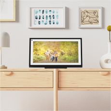 Amazon Echo Show 15 on a console table with framed photos on the wall behind it