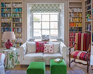 Living room with book lined shelves, sofa, ottomans and striped upholstered chair