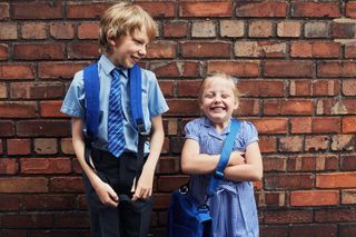 boy and girl smiling stood in school uniform in front of a brick wall