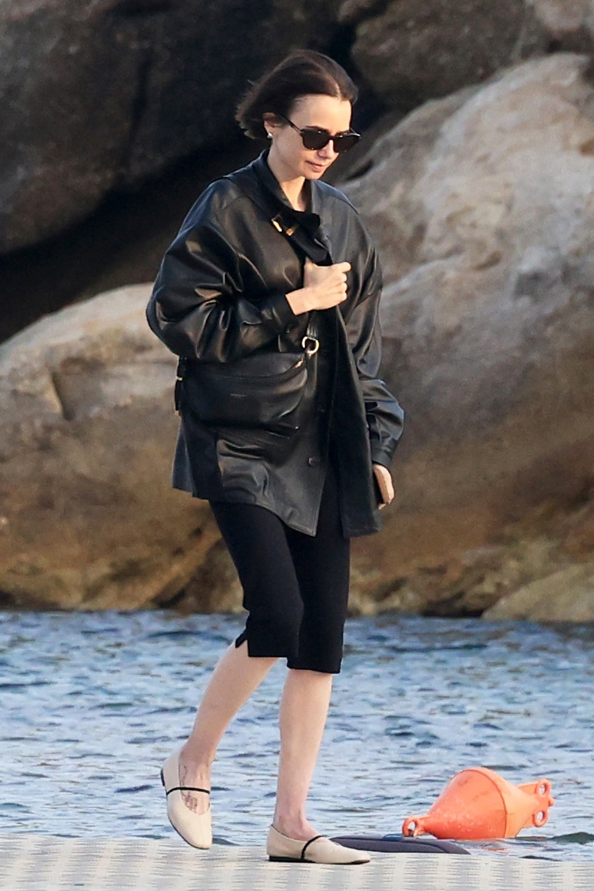 Lilly Collins wearing a black leather jacket, capri pants, and two-tone cream-and-black ballet flats in Mykonos