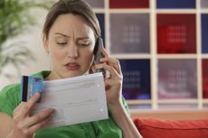 Woman speaking on the phone holding a bill and a credit card 