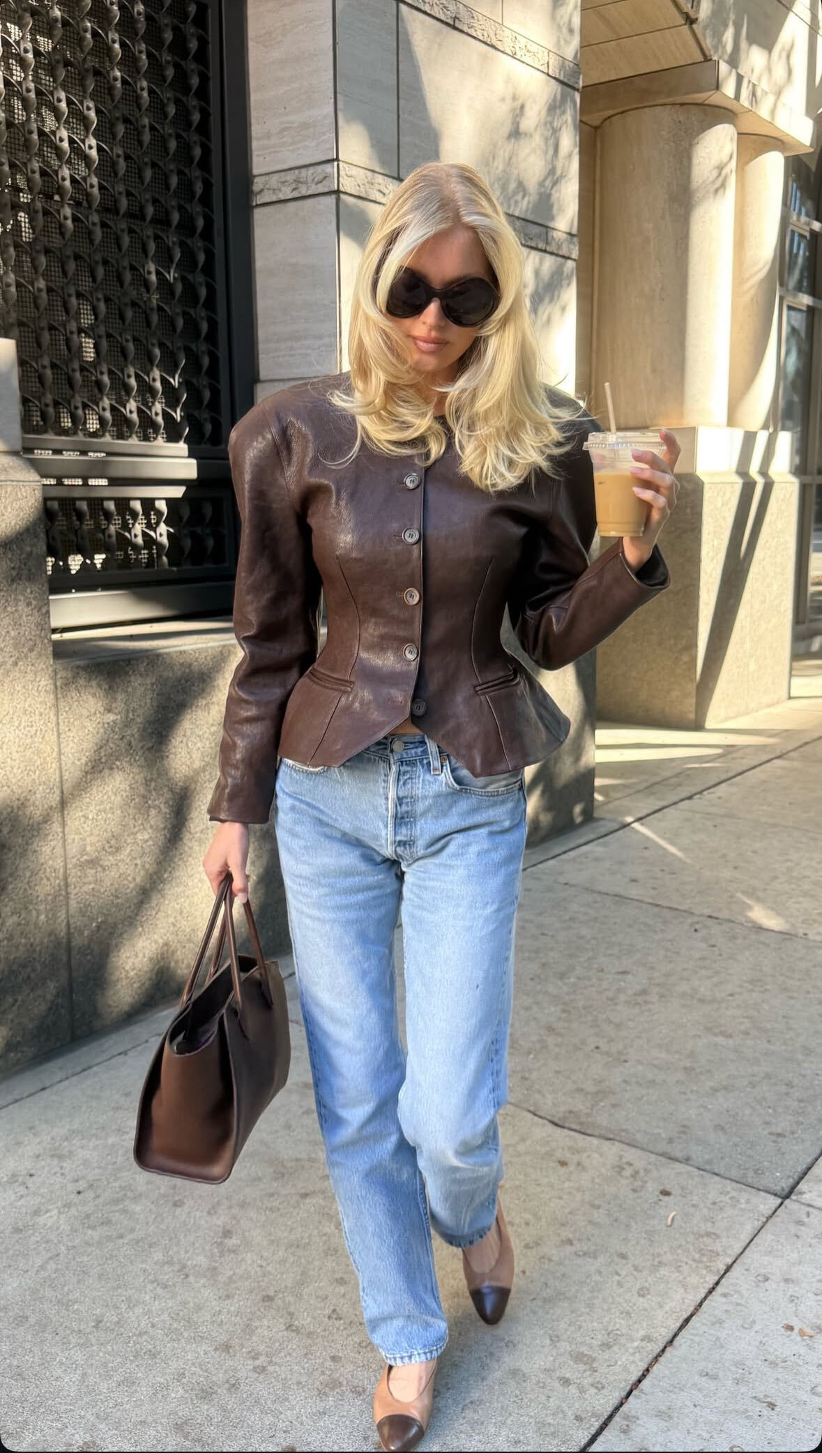 Elsa wears a brown cinch-waist jacket, light-wash jeans, brown tote bag, and two-tone flats.