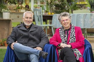 Paul Hollywood and Dame Prue Leith sitting outside, side by side in their coats. 