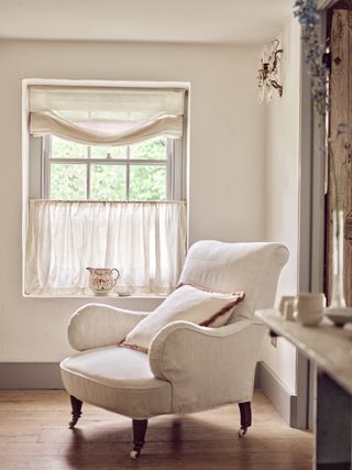 View of a window with sheer linen cafe curtains and a large accent chair