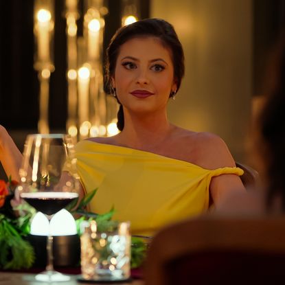 Cara Kies sits at a dining table with a floral arrangement and wine glasses in the 'Million Dollar Secret' finale.