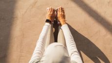 Woman wearing workout clothes stretching down to touch her toes, sitting on stone floor, as part of mobility exercises 