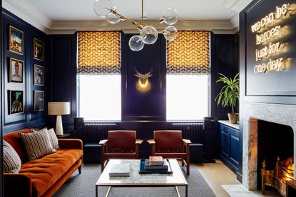 Living room pictures with orange sofa and chairs against a dark purple wall with statement lighting. 