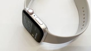 En närbild på sidan av en Apple Watch SE 2 med ett vitt armband som ligger på ett vitt bord.