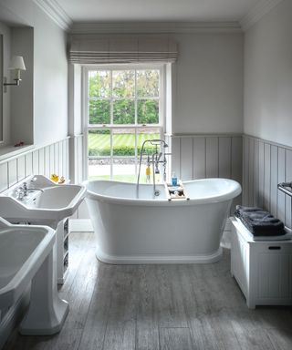 Bathroom with freestanding bath, two basins, and storage bench with grey tongue and groove wall paneling and painted white above