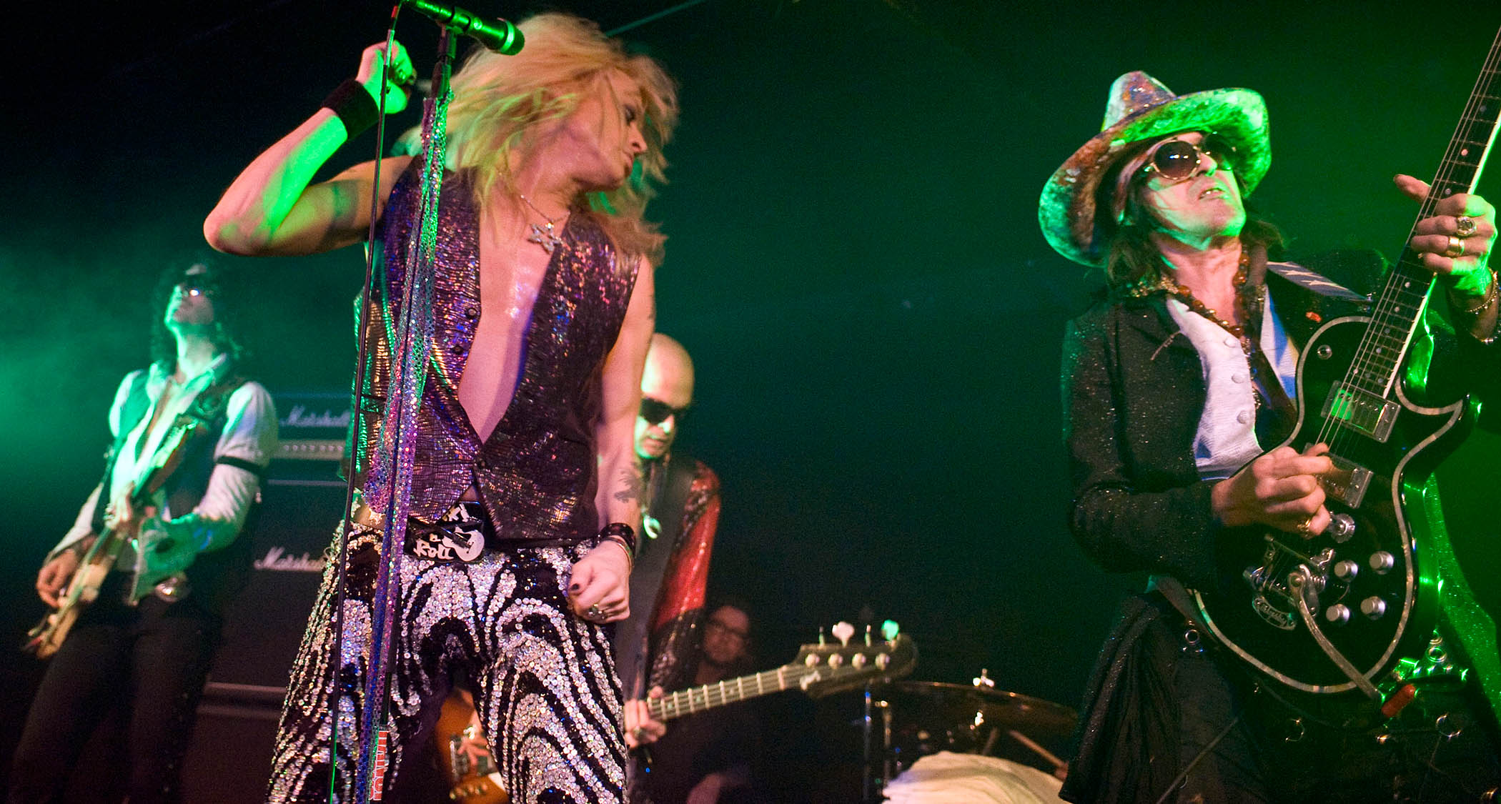 Hanoi Rocks' Michael Monroe and Andy McCoy live onstage. McCory plays a black singlecut and wears dark sunglasses and a wide-brimmed hat.