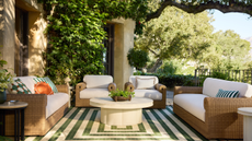 an outdoor patio with a striped rug, a round ottoman, two sofas, two accent chairs, and decorative pillows