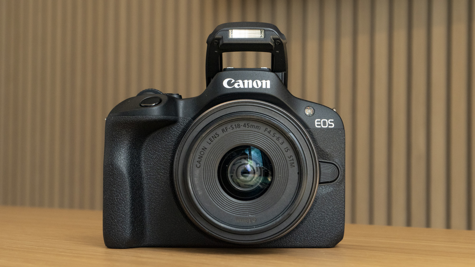 Canon EOS R100 camera on a table front with flash up