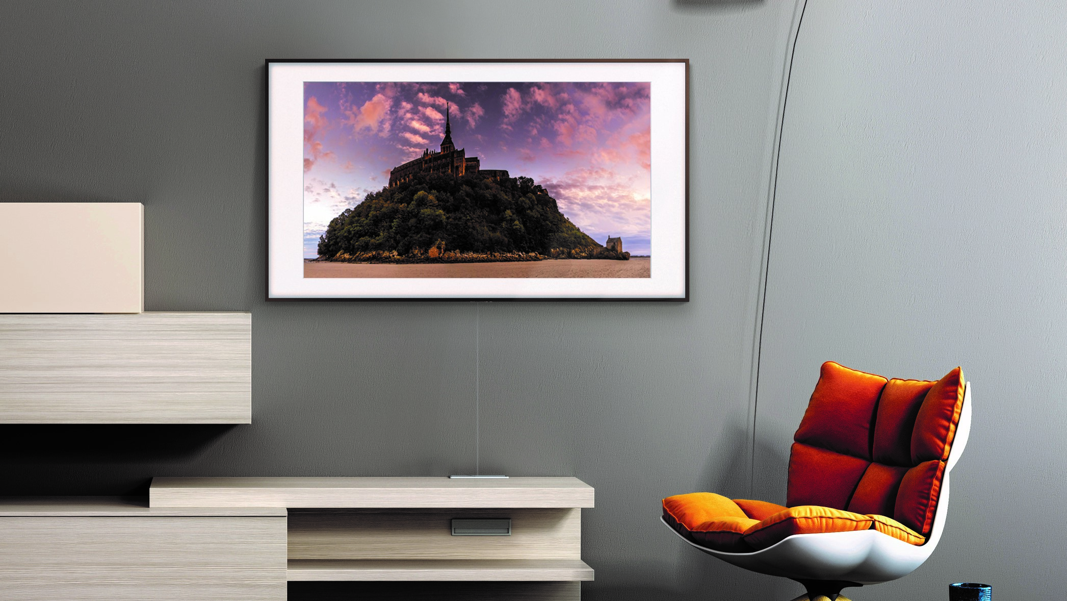Samsung The Frame smart TV hanging on wall while displaying painting, near orange chair