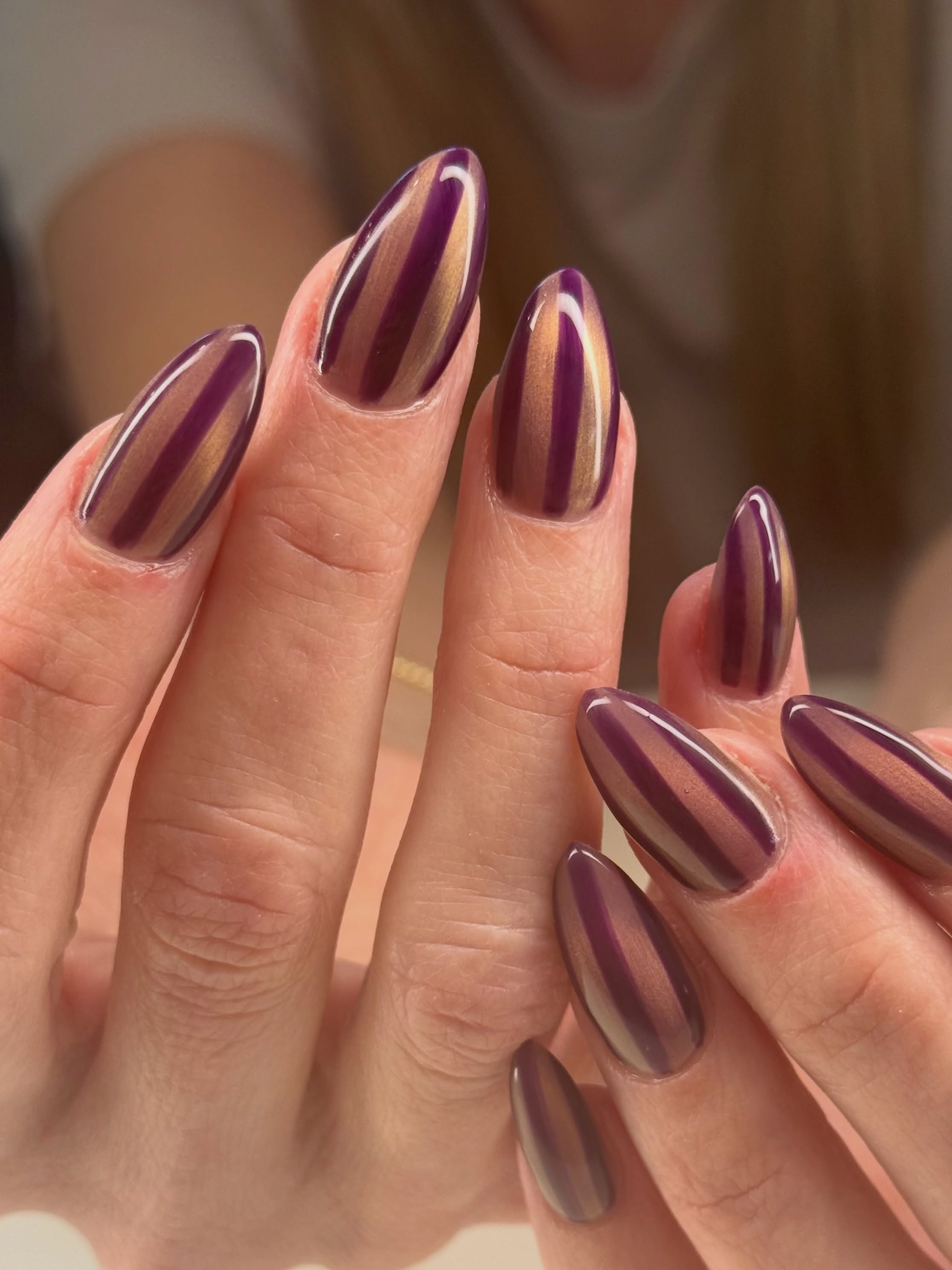 Long almond nails with glossy plum polish broken up by slim vertical strips of negative space