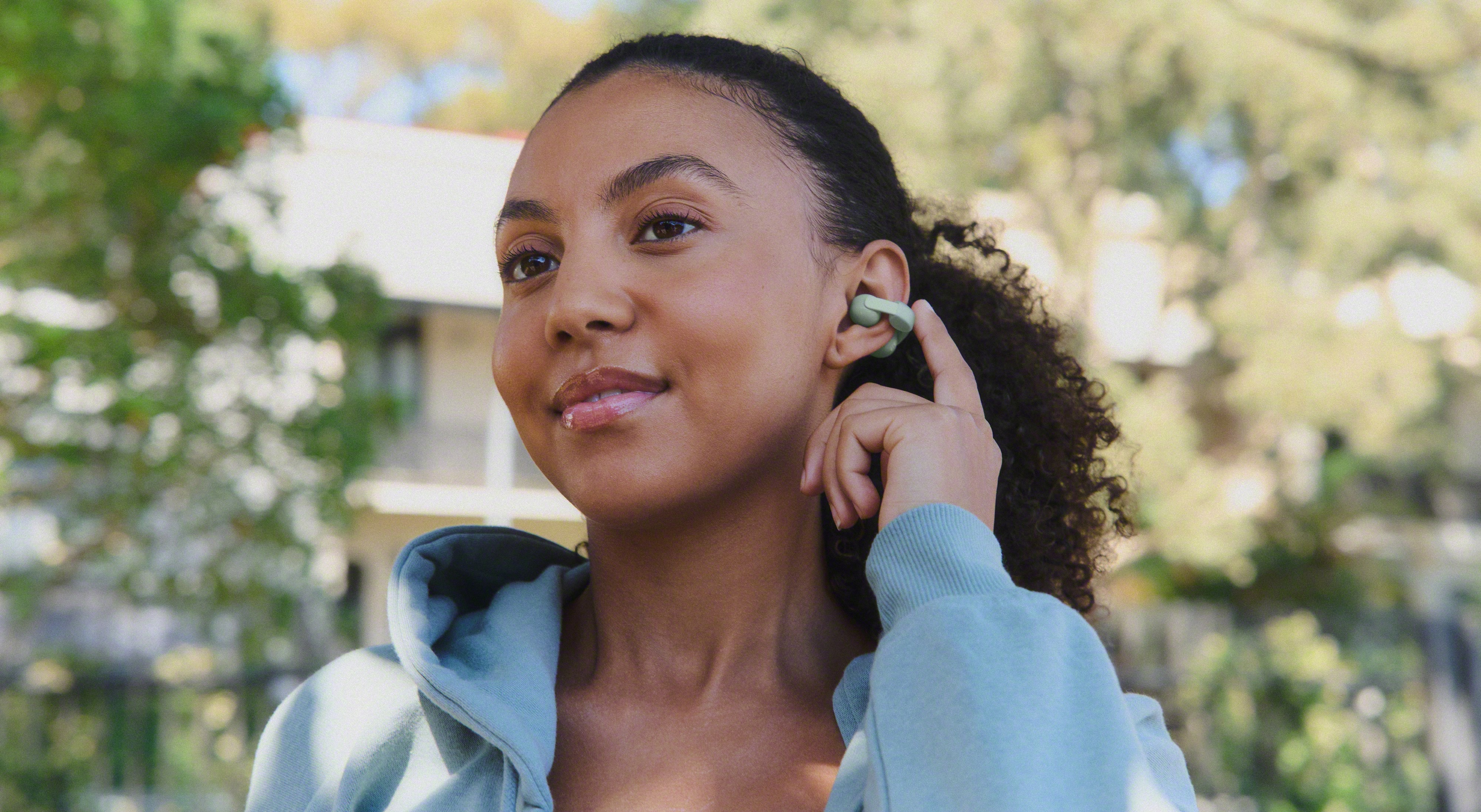 Woman wearing the Sony LinkBuds Clip and touching the left earbud