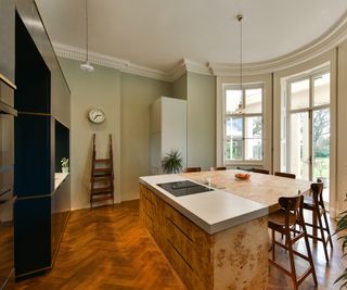 kitchen island with different materials on countertop and base unit in large kitchen with black units and wooden herringbone floor