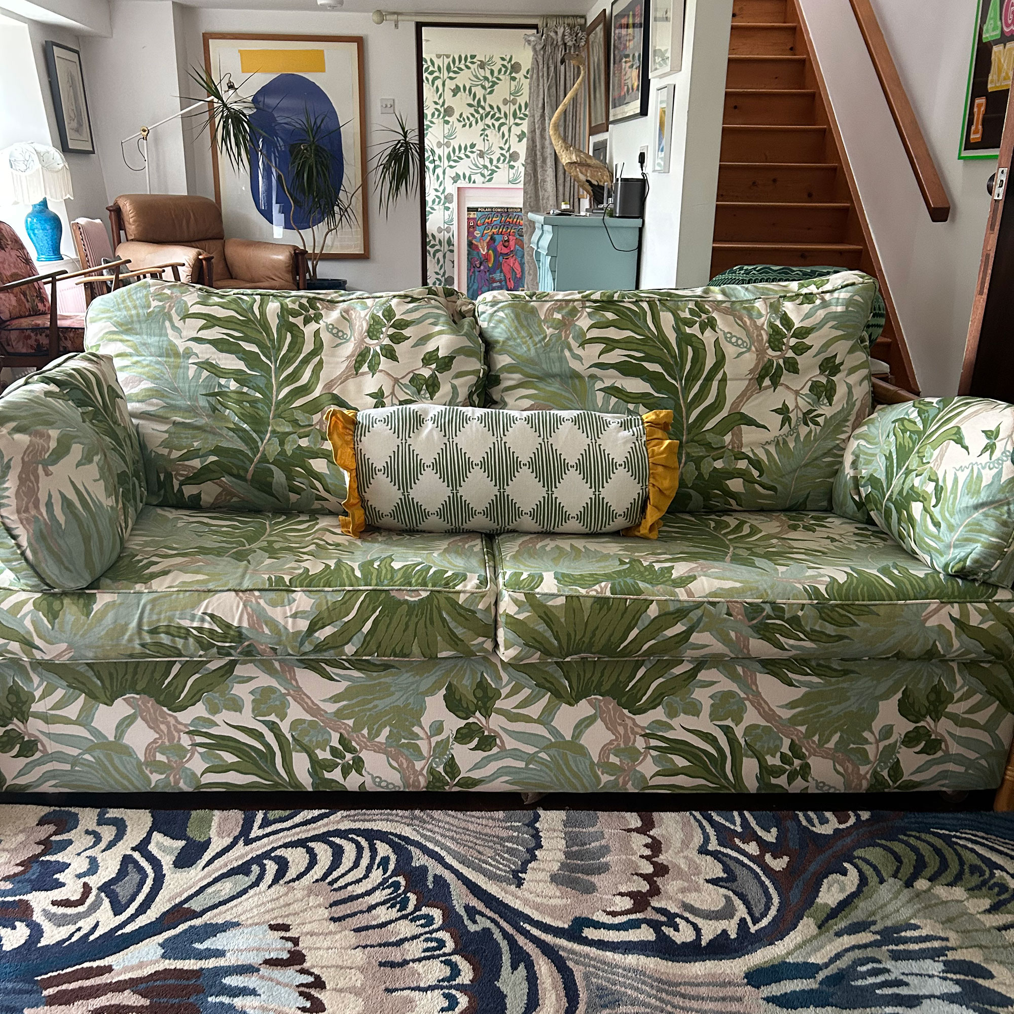 Green botanical patterned sofa with harlequin bolster cushion and blue marbled rug