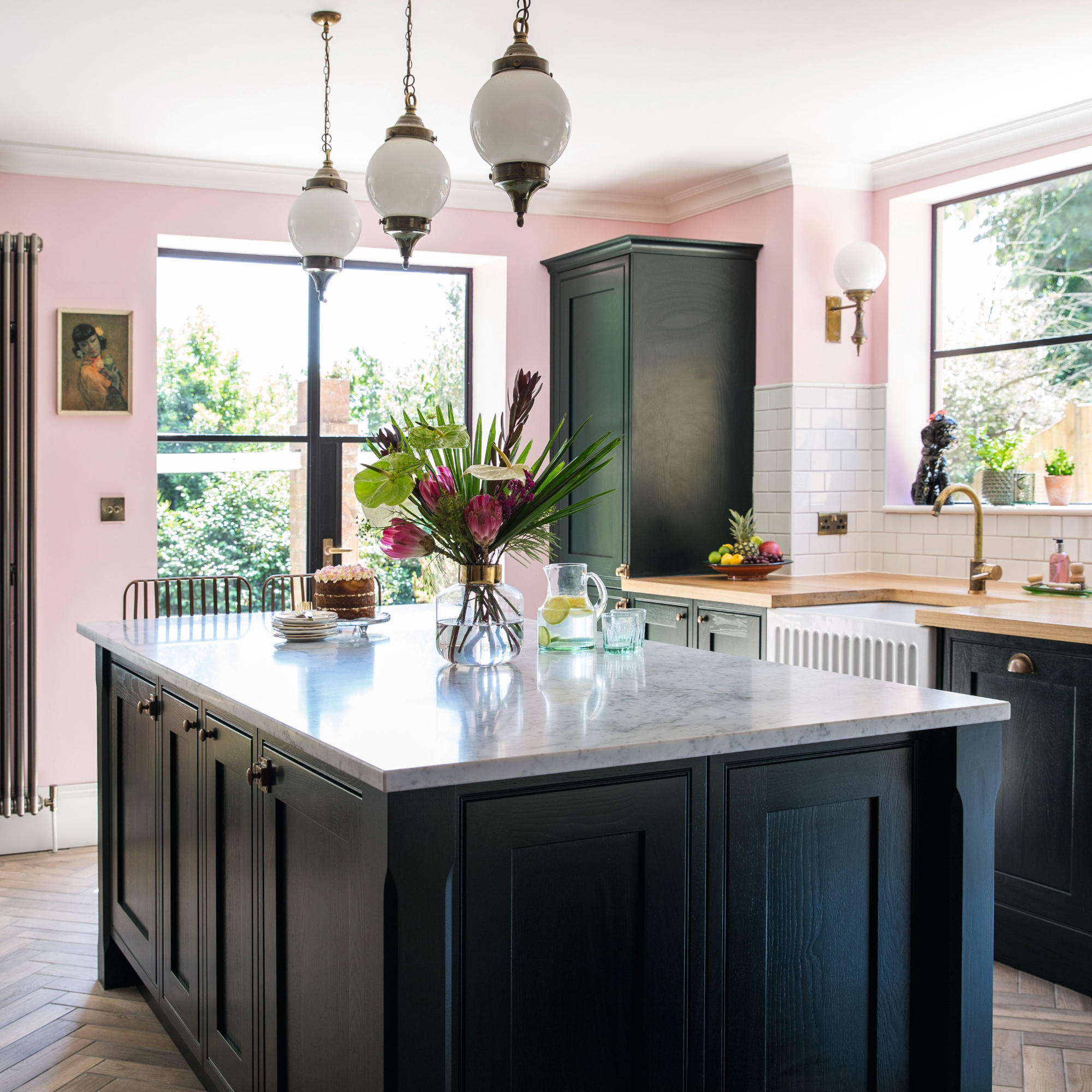Open plan kitchen with pink walls, black Shaker style kitchen units, and rustic vintage furniture