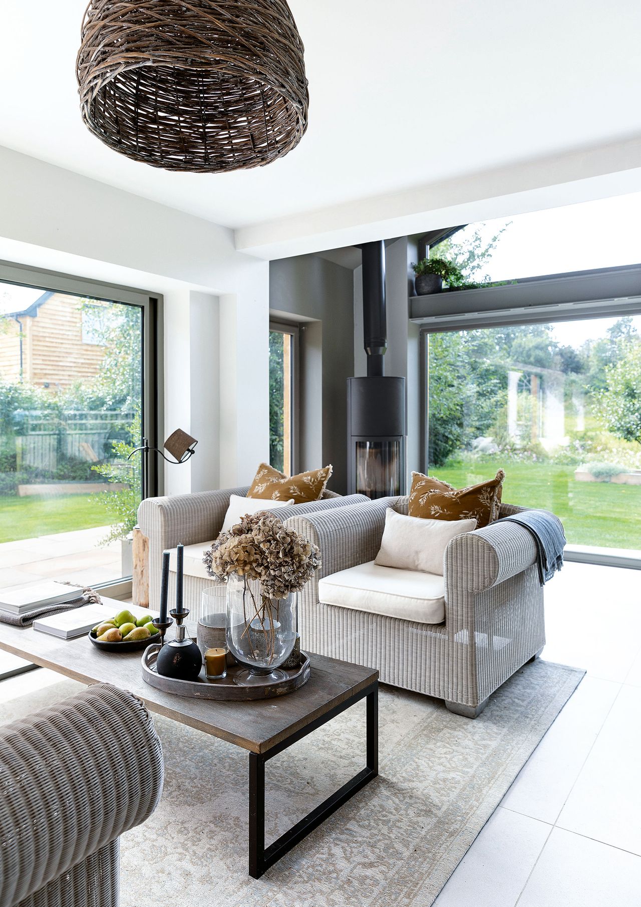 rattan style sofa and coffee table in room with full height glass windows with woodburning stove behind