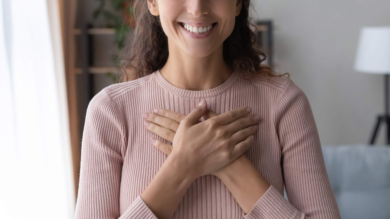 A smiling woman holds her hands on her heart.