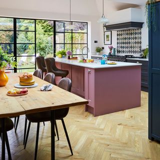 Kitchen-diner area with parquet wood flooring, a wooden dining room table with leather chairs, a pink kitchen island and blue kitchen cabinets