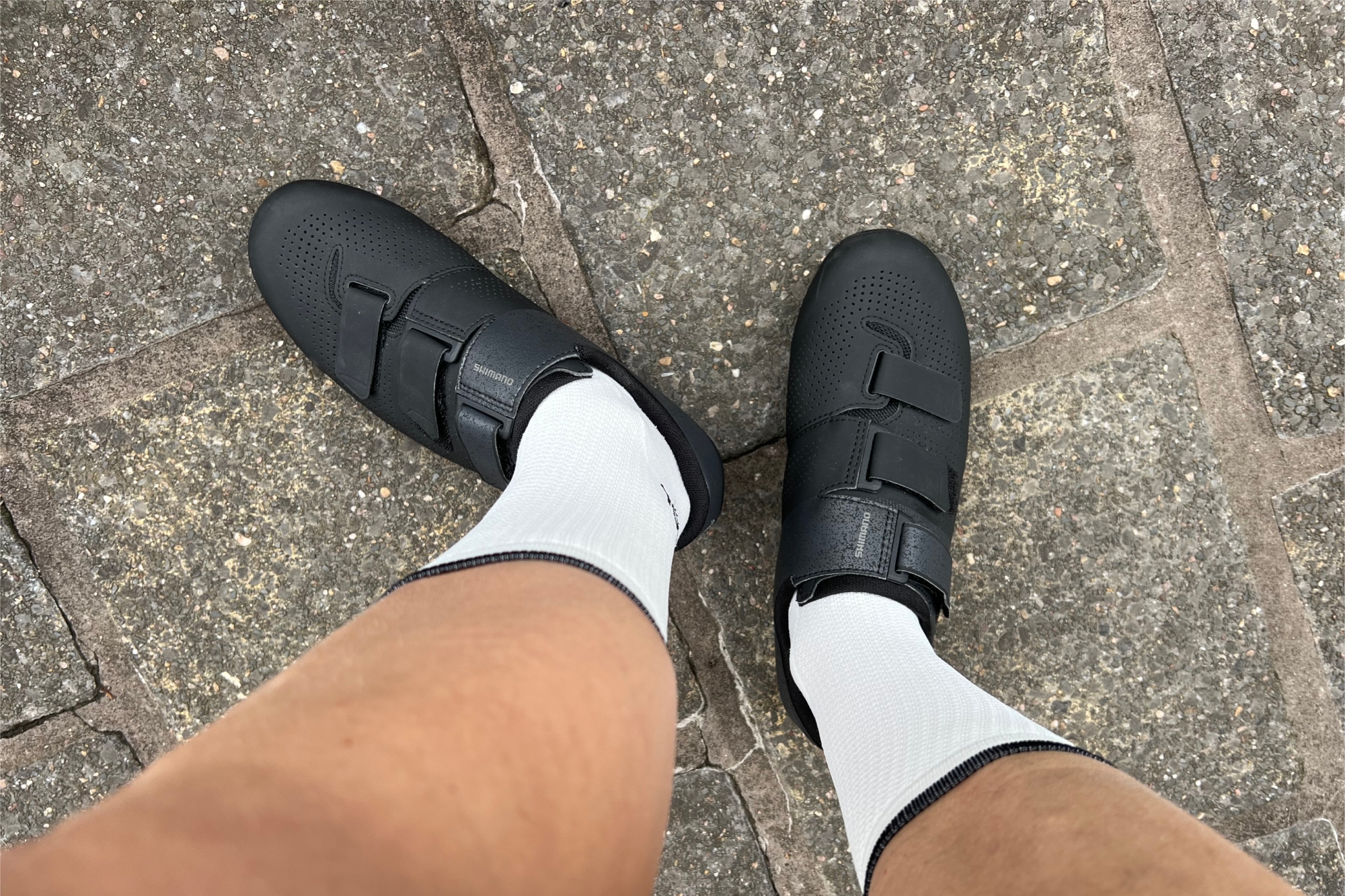 The black Shimano SH-RC102 road cycling shoes paired with white socks on a white womens legs and feet
