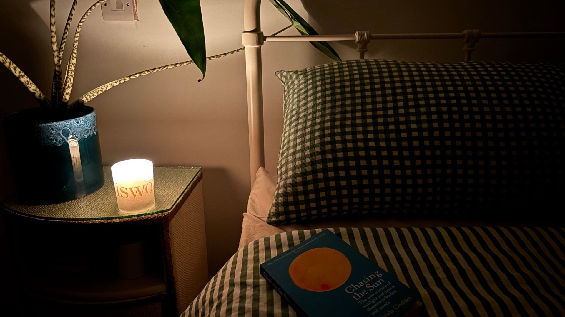 The image shows the left corner of a bed, bathed in candlelight from a nightstand.
