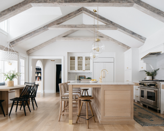 White neutral open plan kitchen space with roof beams and wooden island and table