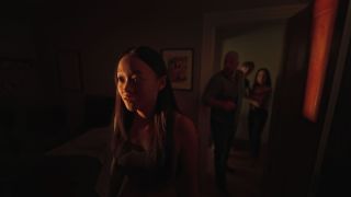 a girl with a surprised expression stands in a dark room as her father, mother, and brother stand behind her in the doorframe