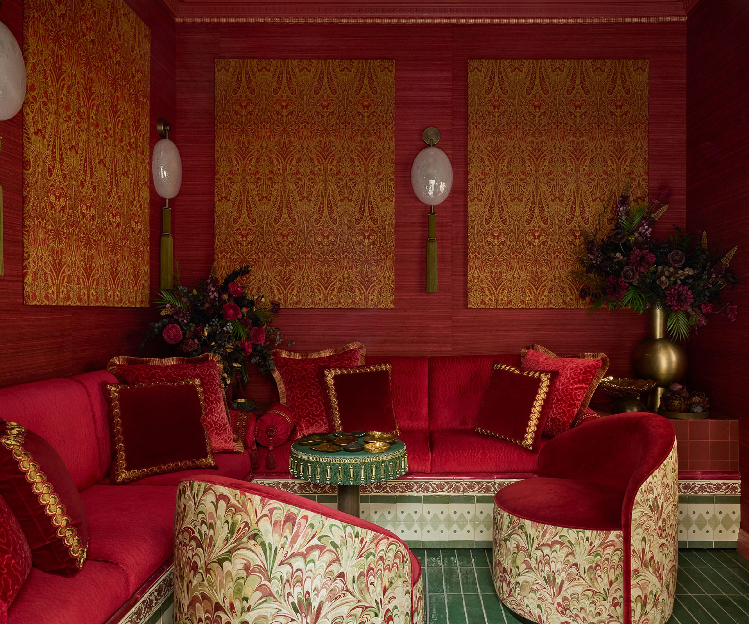 a red grasscloth and fabric wrapped garden room with a tiled banquette seat, green tiled floor and small armchairs for WOW!House 2026