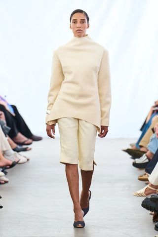 a model walks the runway at Copenhagen Fashion Week wearing beige capri pants