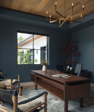 home office painted dark blue with large wooden desk and wood ceiling