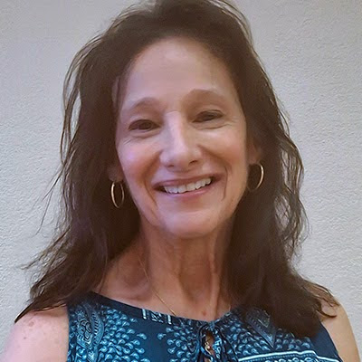 Head and shoulders shot of smiling woman with shoulder-length brown hair, gold hoop earrings and blue patterned top