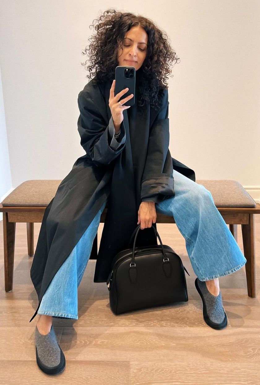 Woman wears black coat, blue jeans, grey shoes and black bag