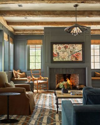 Grey painted living room and fireplace with exposed wooden beams, mustard curtains and window seat cushions