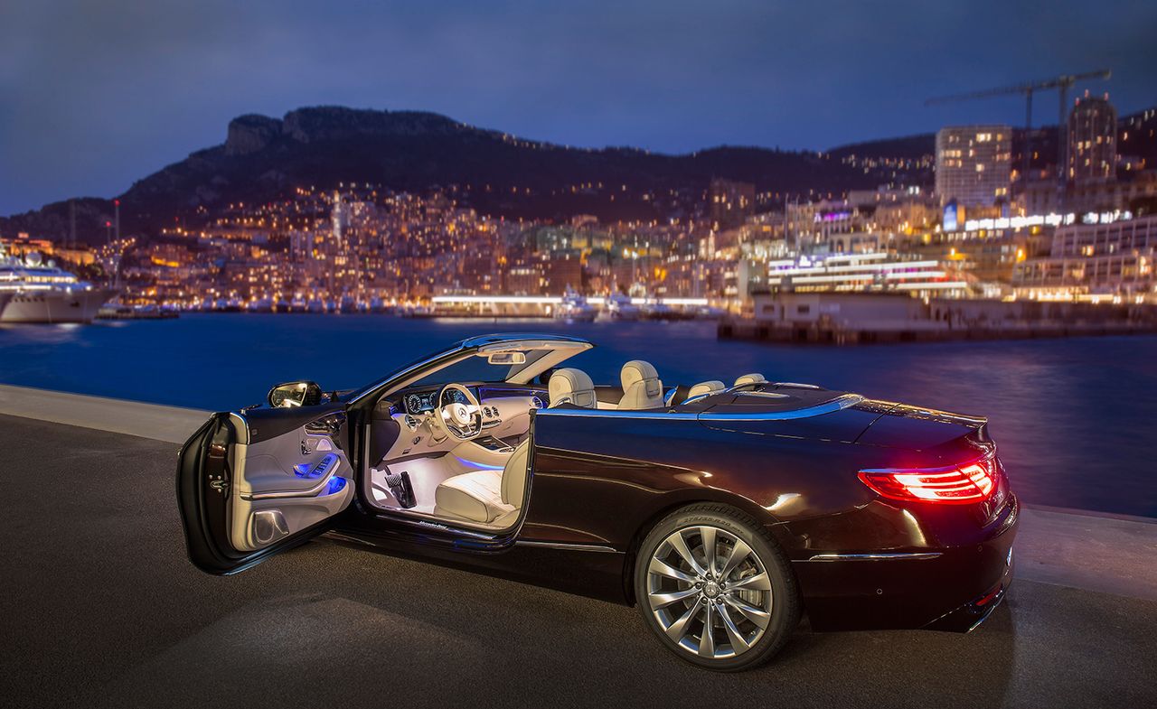 Black sports car with driver&#039;s door open, parked beside a harbour at night